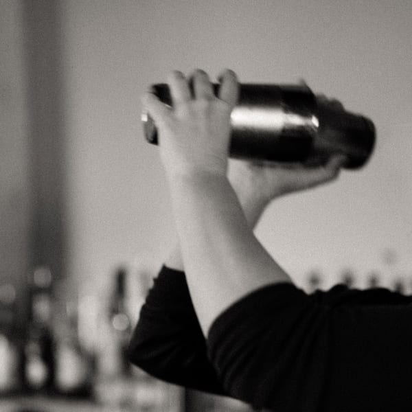 Black and white, blurred image of a bartender shaking a cocktail mixer.