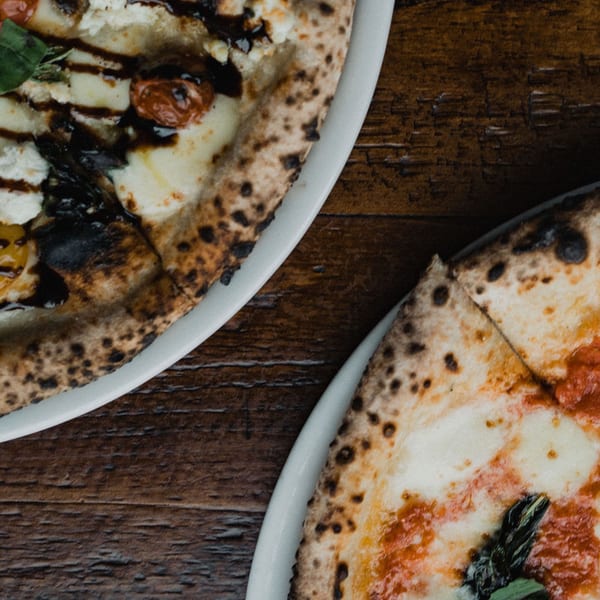 Two Ovn Wood Fired Pizzas, one with balsamic glaze and the other with tomato sauce, on a wooden table.