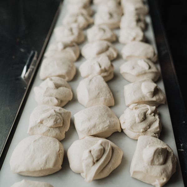 Rows of freshly prepared pizza dough balls resting on a white surface, ready for baking.