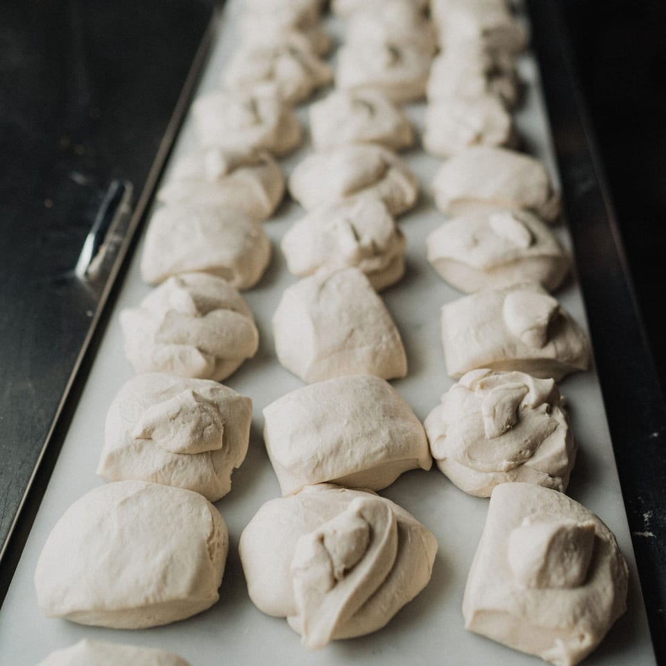 Rows of freshly prepared pizza dough balls resting on a white surface, ready for baking.