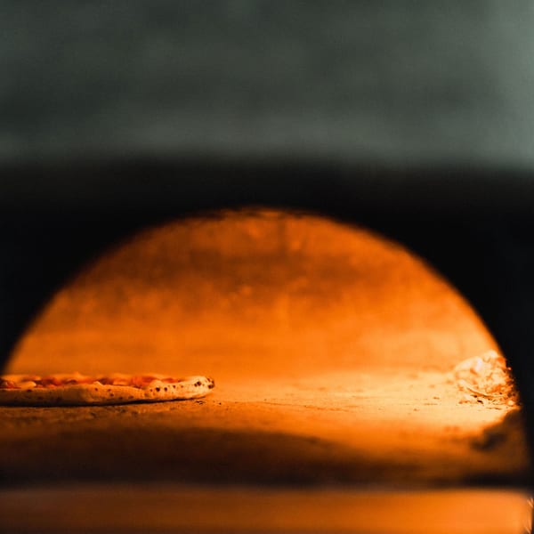 A pizza baking inside a glowing, orange wood-fired oven at Ovn Wood Fired Pizza.