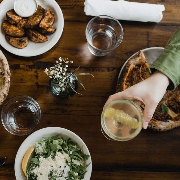 Overhead view of a table with pizza, potato wedges, salad, drinks, and a hand holding a cocktail.
